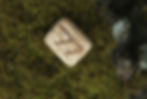 Small rune stone with Ansuz rune (ᚨ) placed on mossy ground, symbol of inspiration and divine communication.