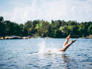 Ein Mensch springt ins Wasser, die Beine und Fußspitzen schauen noch raus