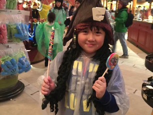 Mia Wang as a young child at Disney land, holding two lollipops and a pirate hat on