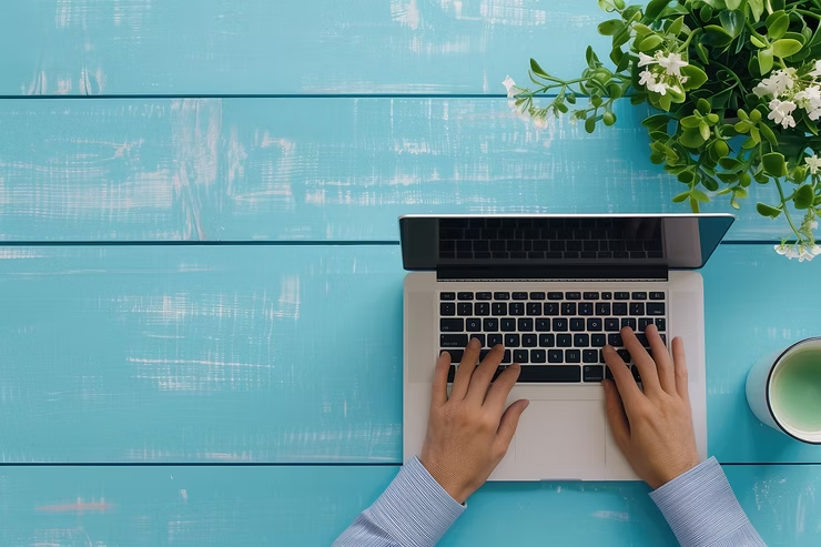 A person typing on a computer on a blue table with a coffee cup to the right.