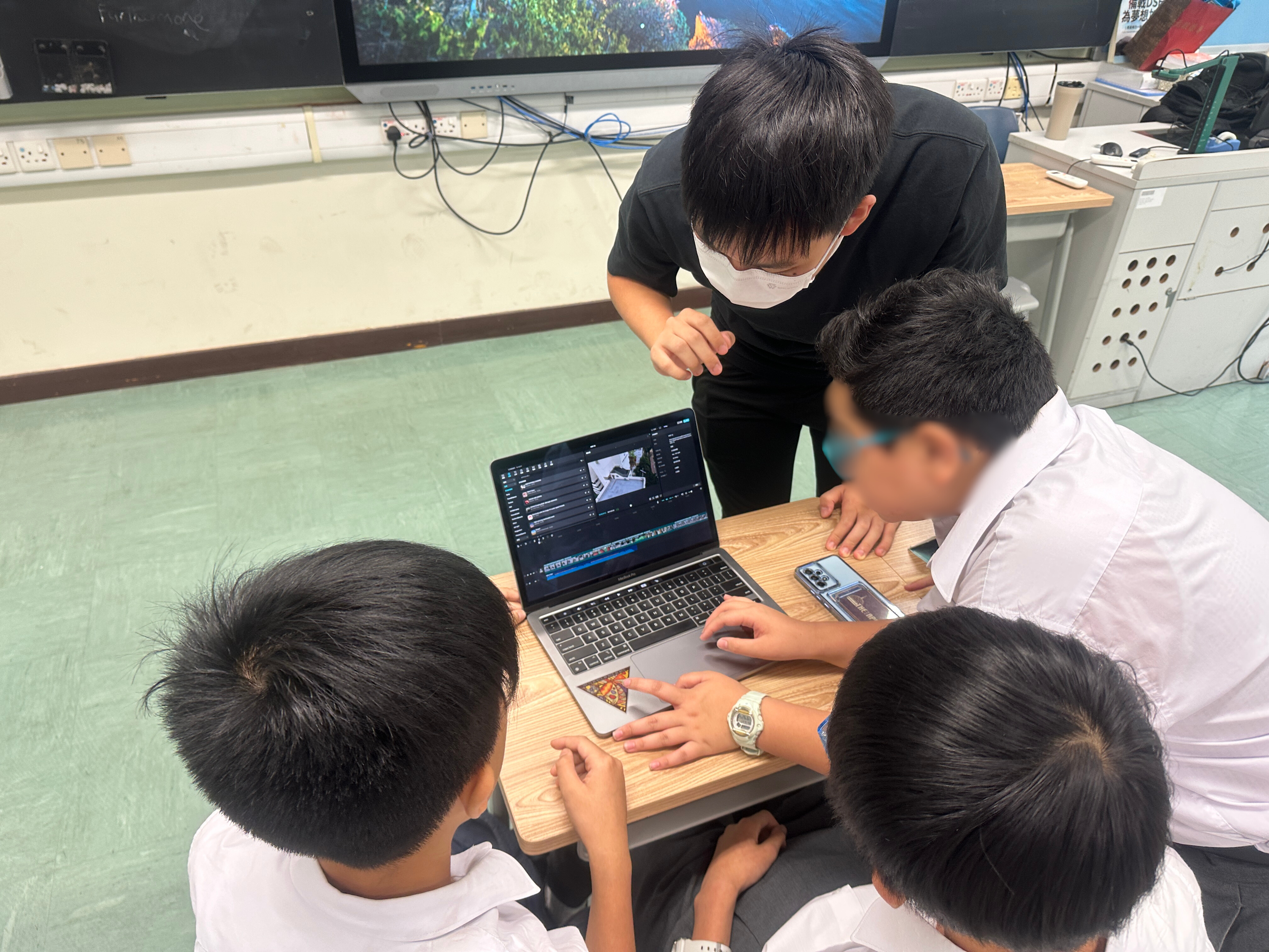 三名學生坐在教室桌前進行短片剪接