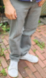 A photo of a man from the hips down wearing grey jeans and white Be Lenka minimalist shoes.