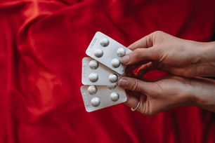 Two hands hold three blister packs of misoprostol pills in front of a red fabric background.