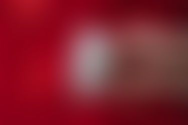 Two hands hold three blister packs of misoprostol pills in front of a red fabric background.