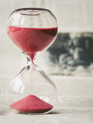 An hour glass filled with red sand trickling down.