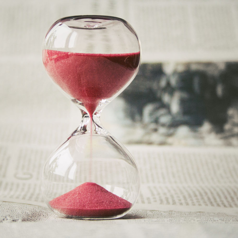 A photo of an hour glass timer with red sand falling down.