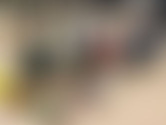 A smiling person kneels beside various percussion instruments on a wooden floor, including drums, maracas, and xylophones, in a bright room.