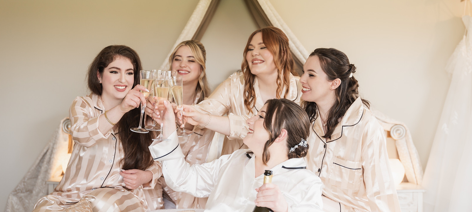 bridal party celebrating on the wedding morning in their silk champagne coloured matching pyjamas toasting with champagne with glamourous makeup.
