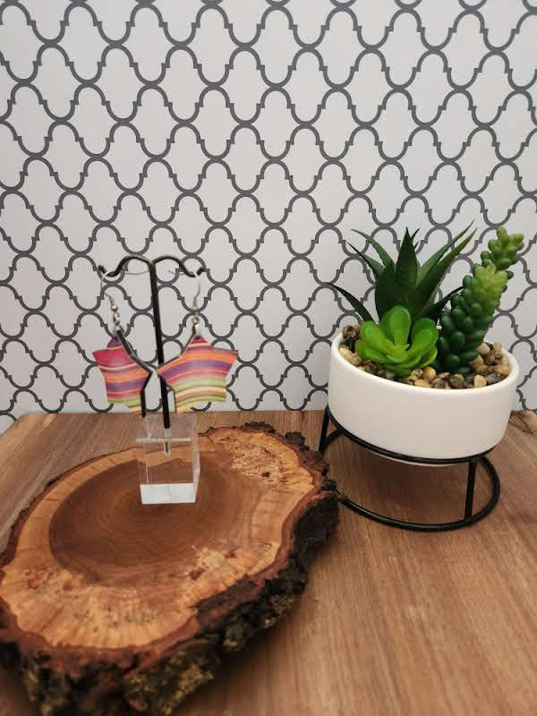 Thumbnail: Earrings are hanging on an earring tree sitting atop a live edge piece of wood, next to a cream planter with green succulents