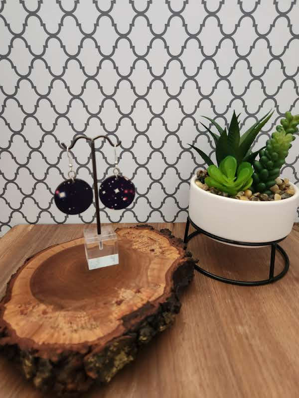Thumbnail: Earrings hanging on earring tree atop a piece of live edge wood next to a cream planter containing green succulents