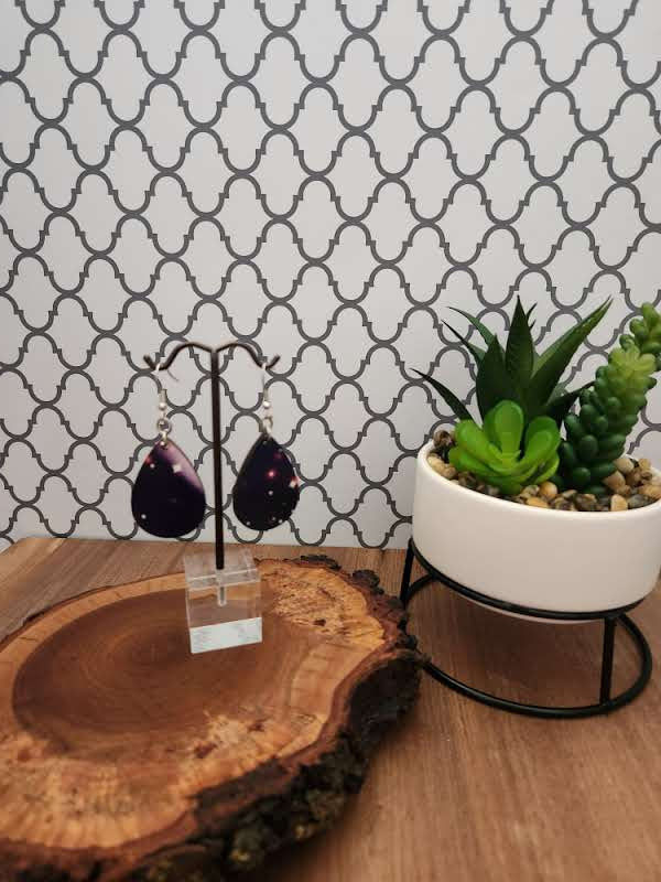 Thumbnail: Earrings hanging on earring tree atop a piece of live edge wood next to a cream planter containing green succulents