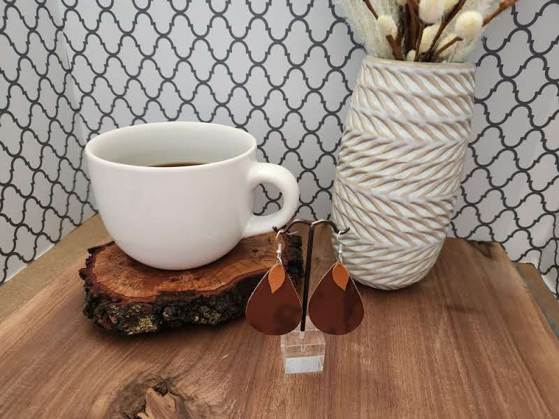 Thumbnail: earrings are on earring tree next to white coffee cup sitting on live edge wood in front of ceramic cream vase with willows