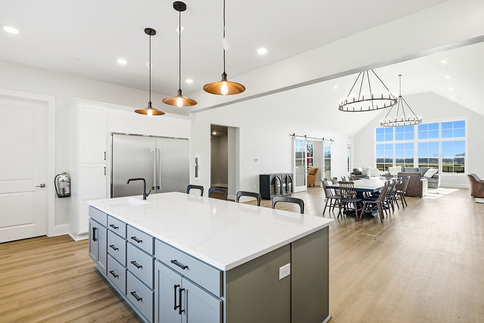 Spacious kitchen-living room with large windows, pendant lights, white island with sink, gray cabinets, dining table, and cozy seating.