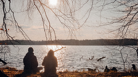 back view of two people sitting by a lovely lake 