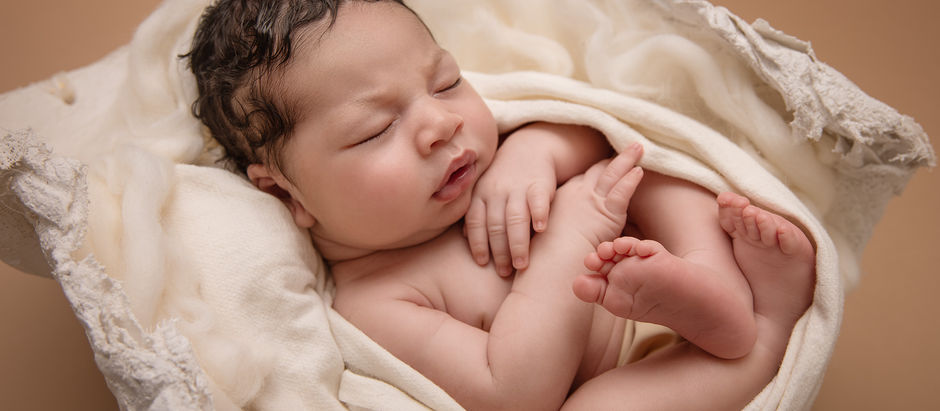 newborn portrait of a baby boy swaddled in white fabric sleeping and tucked into his moms' plaster belly cast from her pregnancy with him