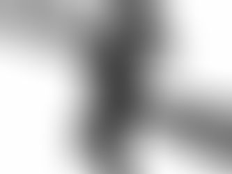 Pregnant woman poses for maternity portraits draped in black fabric against a white backdrop with one hand on the small of her back and the other on the top of her head with her hair flowing behind her