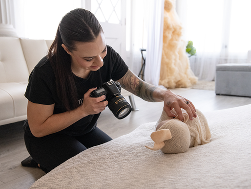 Newborn photographer Ashlie Bradley posing a newborn baby in her studio and smiling with her camera in one hand