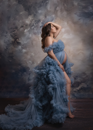 pregnant woman wearing a blue tulle maternity dress with ruffles posing to the side with one hand on her head the other on the top of her thigh