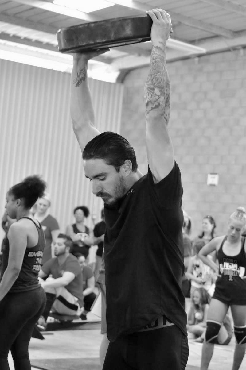 Well muscled man standing with a weight over his head in a functional fitness competition