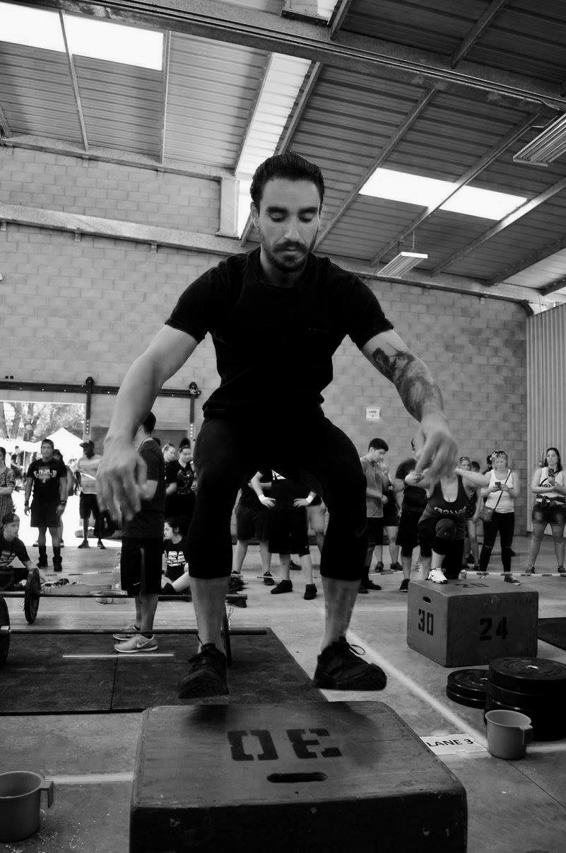 Well muscled man jumping onto a plyometric box in a functional fitness competition