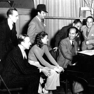 Produção do filme "Shall We Dance" (1937). Em pé: Diretor de dança Hermes Pan, diretor Mark Sanmdrich, Ira Gershwin. Sentados: Fred Astaire, Ginger Rogers e George Gershwin (ao piano). Fotografia.