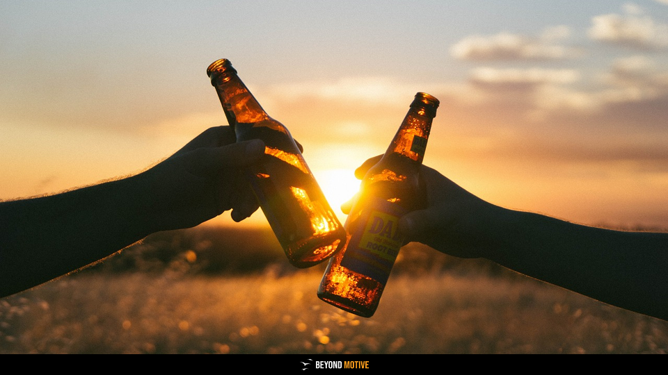 Two hands clinking beer bottles at sunset