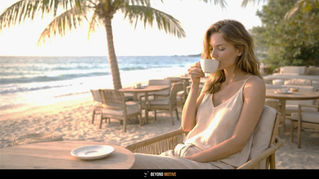 Woman in light dress sipping from a cup by the beach. Palm trees, ocean, and sandy chairs create a peaceful, sunny ambiance. The Art of Slow Travel: How to Explore the World at Your Own Pace