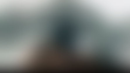 Person in black jacket sits on a rocky cliff with arms outstretched, surrounded by misty mountains. Text reads "Beyond Motive." Serene mood. How Living in the Present Moment Can Transform Your Life