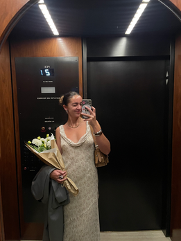 Girl taking a mirror selfie in a NYC elevator; flowers in hand.
