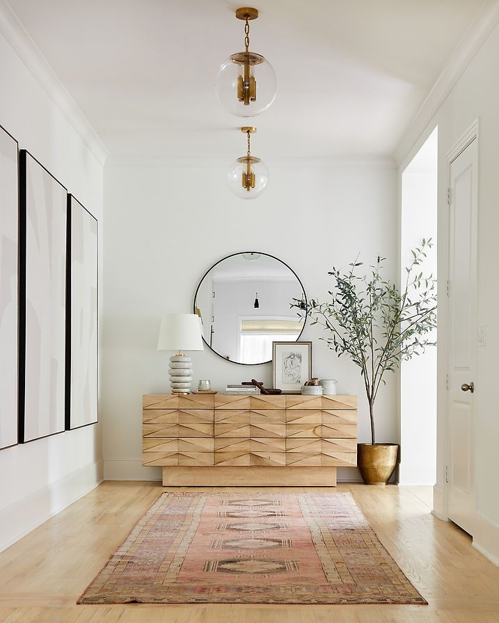 Hallway design with repeating brass pendants, round mirror, oversized artwork, and vintage