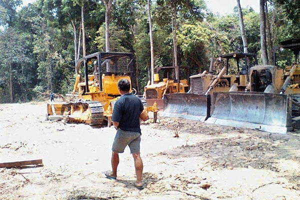 A Lao villager walks by bulldozers belonging to a Chinese-backed company that is clearing land to build cattle farms in Champhone district of Savannakhet province in southern Laos, June 2016. (Photo: RFA)