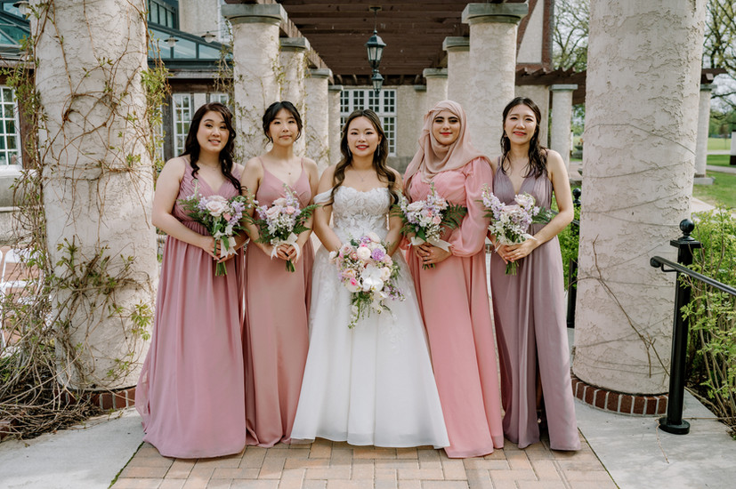 A Bride and Bridesmaid pose outside of the Assiniboine Park Pavillion with beautiful flowers