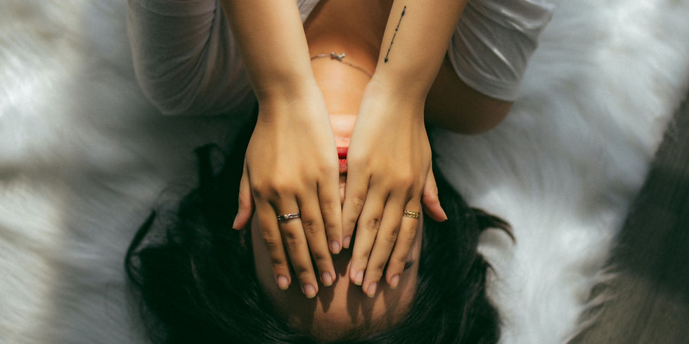 A woman lies back on a bed, hands covering her face in stress