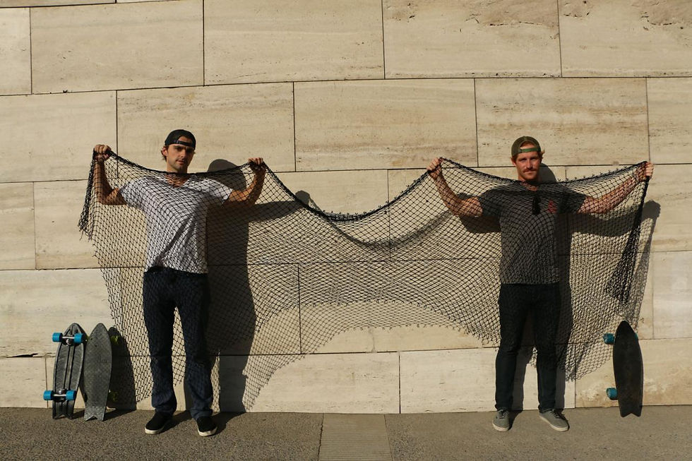 two men in t-shirts and backwards hats holding up a fishing net, which they reuse to make recycled plastic skateboards.