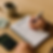 A person writing a budget plan in a notebook with a calculator and cash on the table.