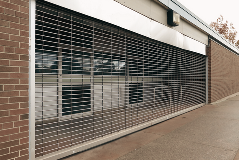 A silver security gate covering a large opening on a storefront in Winnipeg, Manitoba, after being installed by M.A.N. Property Protection Solutions.