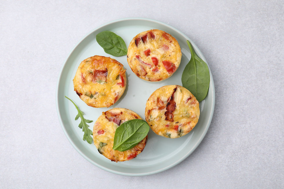Four mini vegetable egg muffins on a pale blue plate with spinach leaves, shot on a light white background.