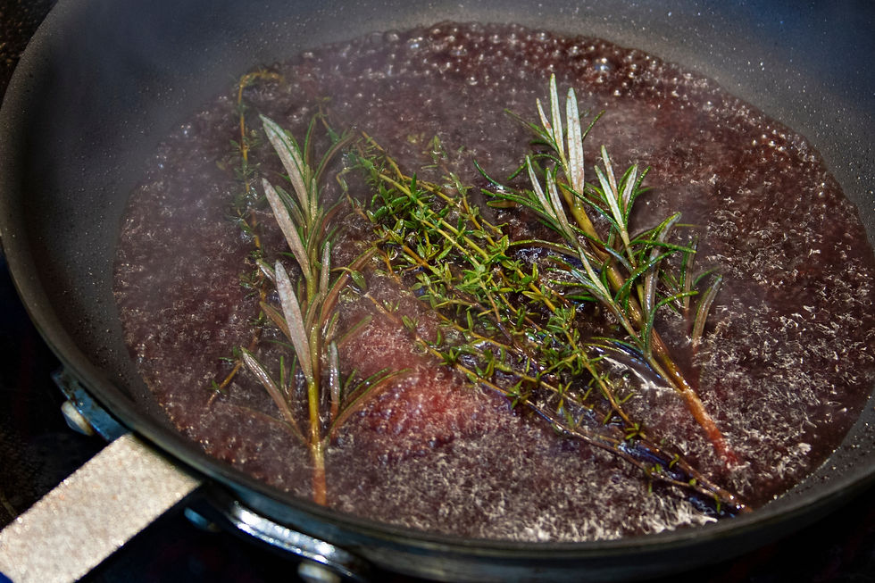 Boiling dark sauce in a saucepan with rosemary and thyme sprigs on a stovetop.