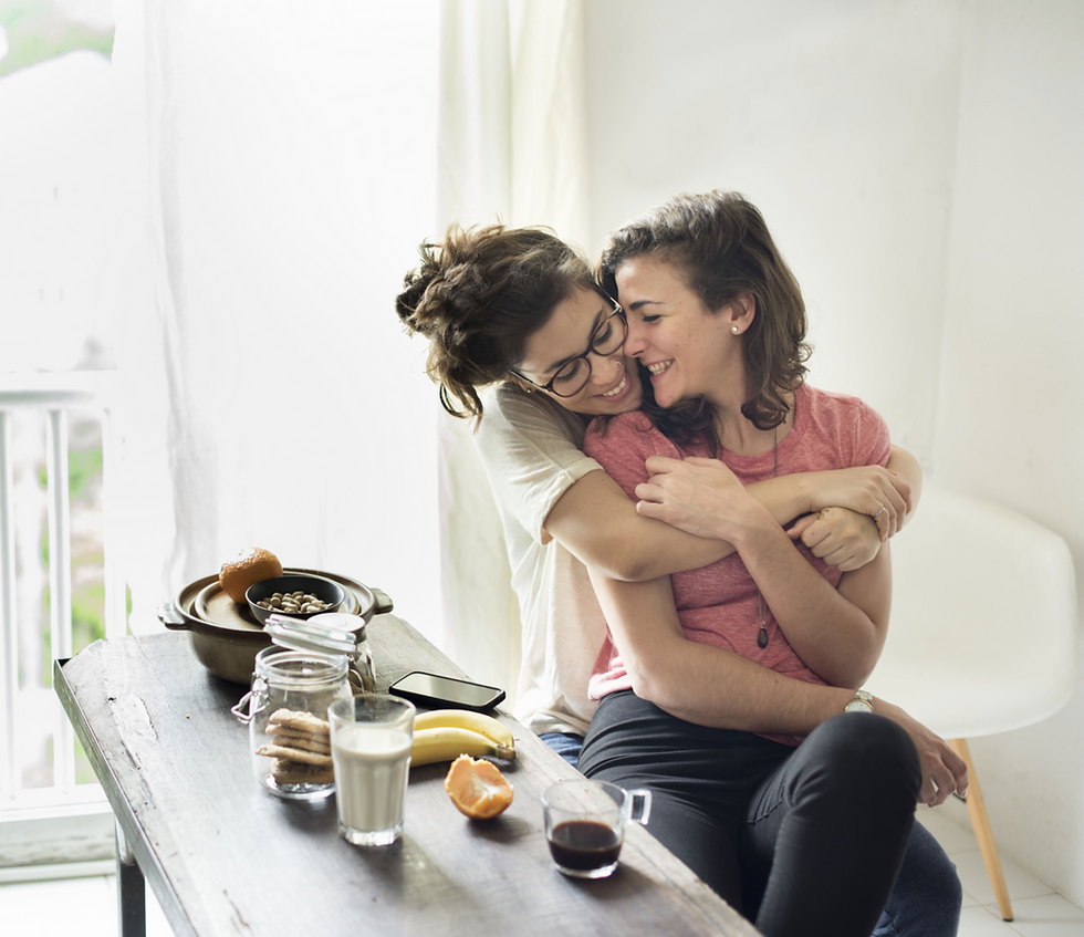 Happy Lesbian couple hugging in the kitchen while having breakfast.