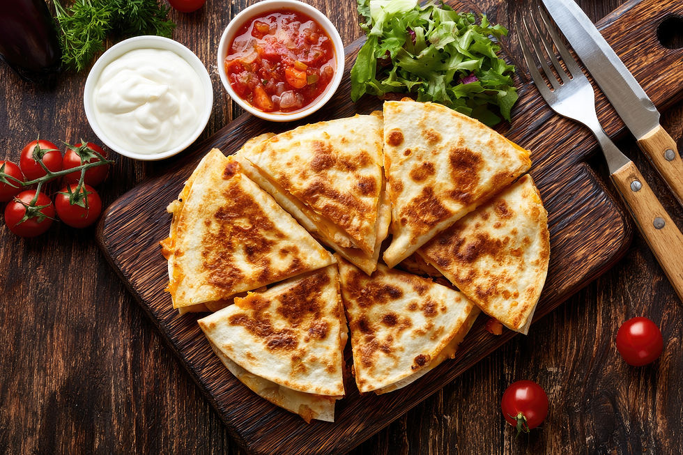 Quesadilla wedges on a wooden board with salsa, sour cream, greens, tomatoes, and knife and fork on a rustic table.