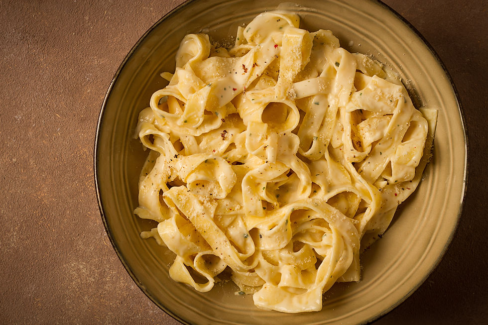 Creamy fettuccine pasta with grated cheese and pepper on a tan plate, photographed from above on a brown tabletop.