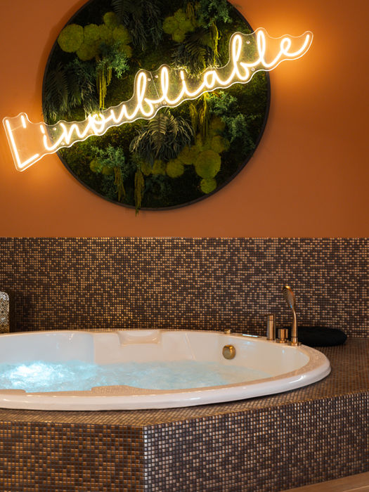 White bathtub with gold accents, neon sign reads L'inoubliable. L'inoubliable Chambre.