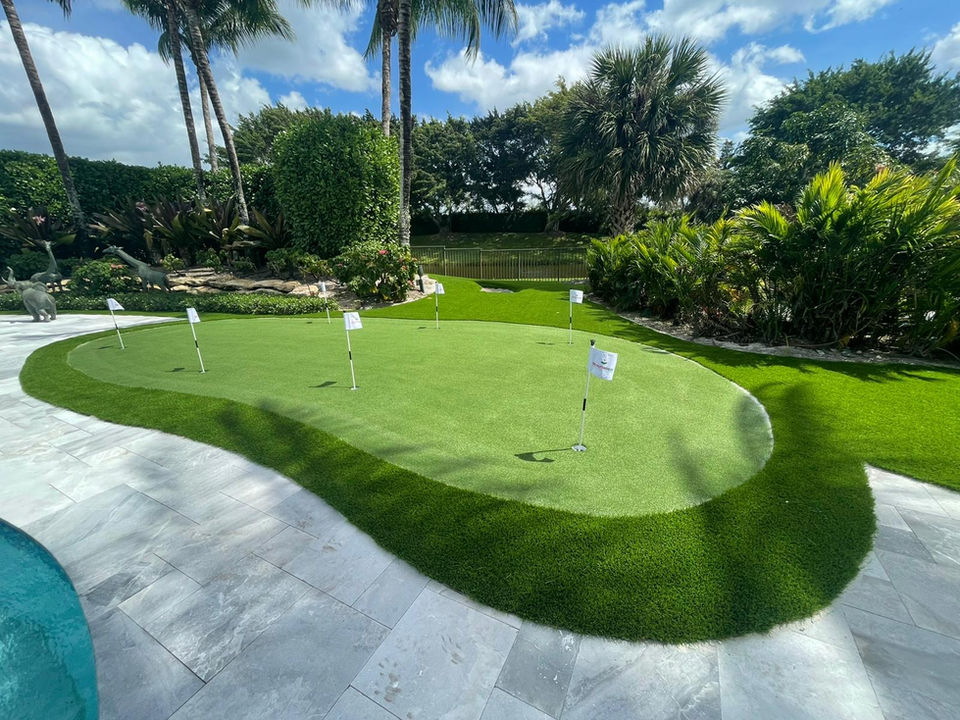Custom backyard putting green with synthetic grass, golf flags, and tropical foliage, perfect for home practice in florida.