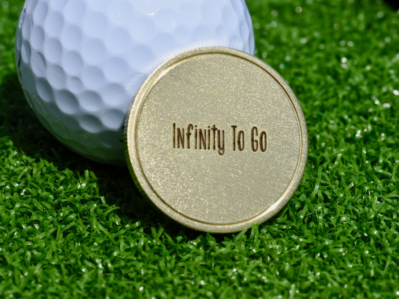Bronze anniversary golf marker resting on a grass surface beside a golf ball and tee.