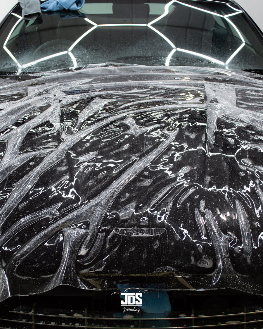 Paint protection film being laid wet onto a black bonnet under the hexagon lights