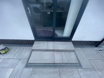 Close-up of porcelain patio slabs with threshold drain near glass door