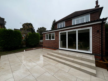 Large garden paved with sandstone slabs outside a red-brick house.