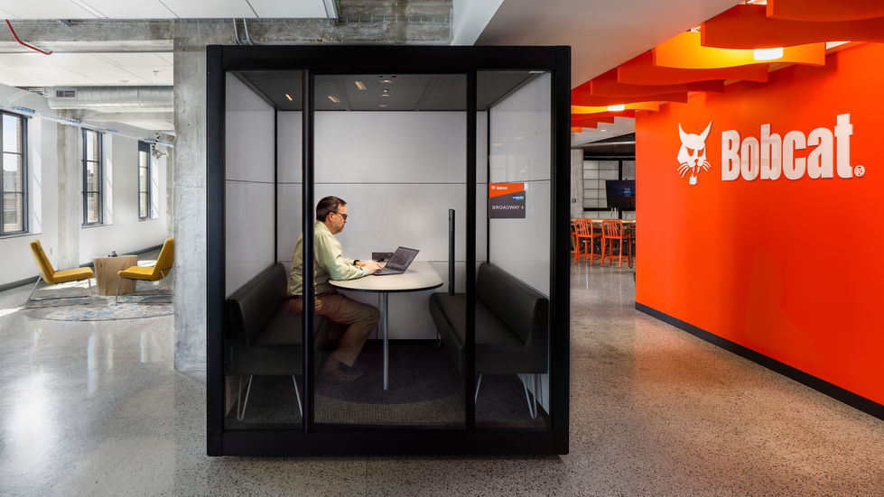 A person sitting at a desk in a glass meeting booth. 