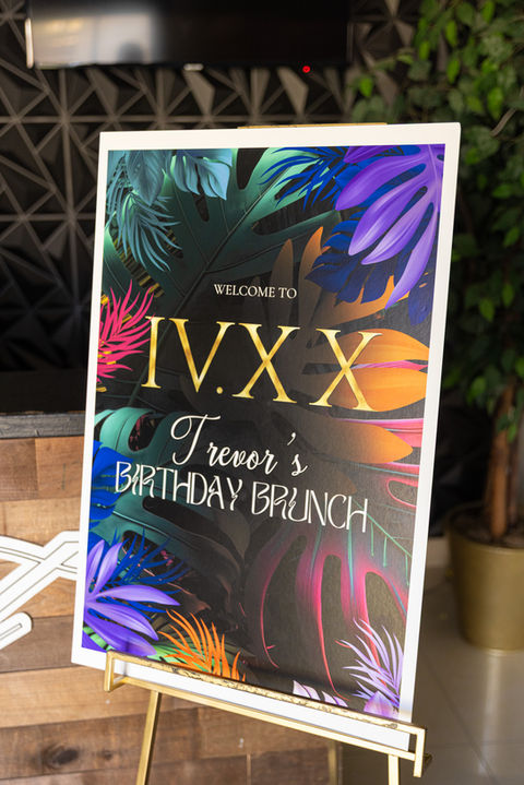 A tropical-themed welcome sign that says "Trevor's Birthday Brunch."