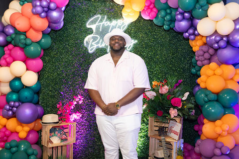 Trevor posing in front of a happy birthday sign and a tropical-themed backdrop.